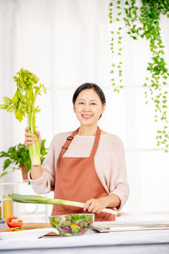 手拿芹菜在厨房做饭的中老年女性