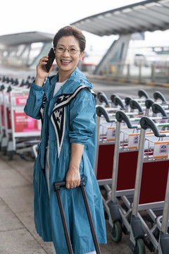 老年女人在机场拉着行李箱打电话