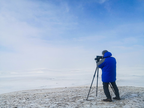 冬季雪原三脚架照相机男人背影