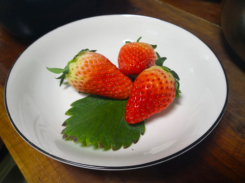 白色盘子里红色草莓绿叶