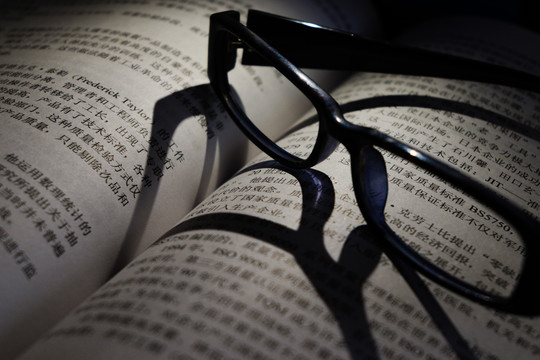 灯光下打开的书本上放着眼镜