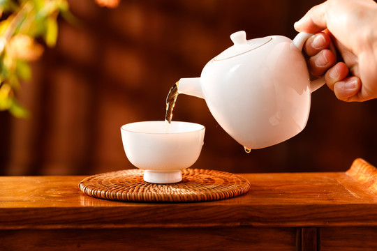 人拿着白色茶壶向茶杯倒茶