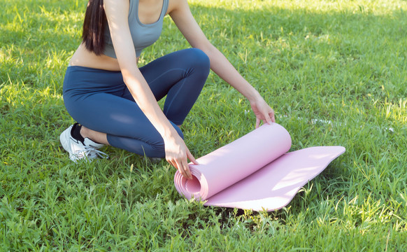 草地上整理瑜伽垫的女性