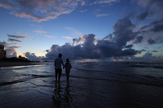 爸爸牵着女儿的手在海边看日出