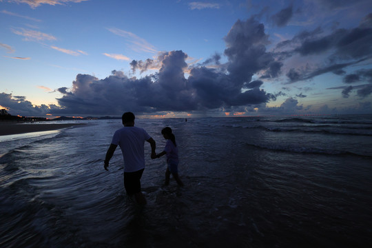爸爸牵着女儿的手在海边看日出