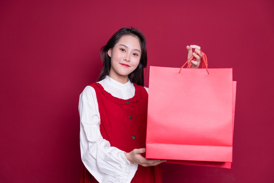 红背景手持购物袋的年轻女性