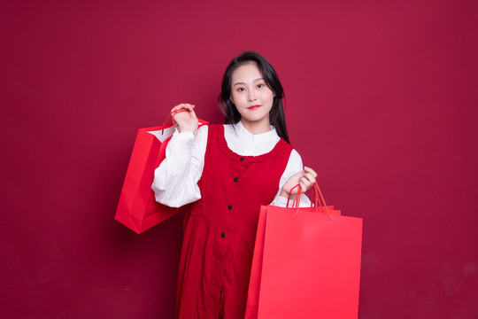 红背景手持购物袋的年轻女性