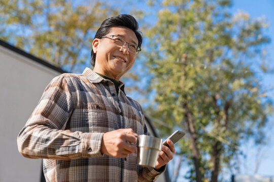 一个老年男人站在房车前拿着手机喝咖啡