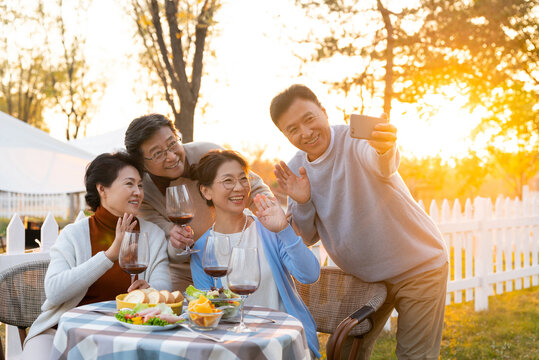 夕阳下中老年朋友在庭院里聚会喝酒拍照片