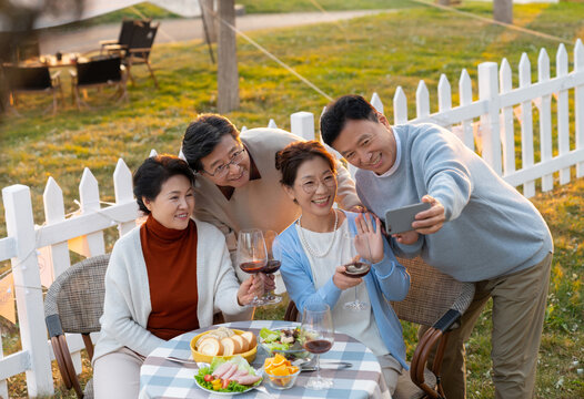 夕阳下中老年朋友在庭院里聚会喝酒拍照片