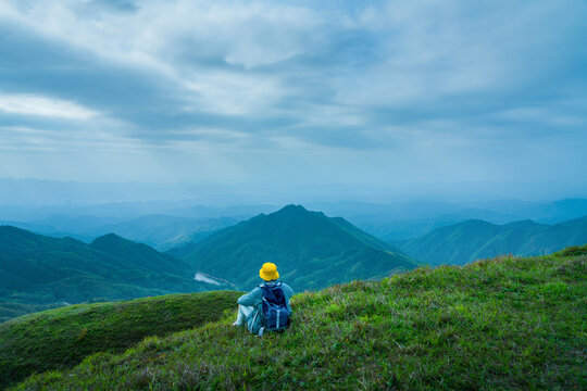 一个人徒步坐在山顶远眺山河