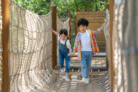 两个小孩子相互鼓励牵手走绳桥