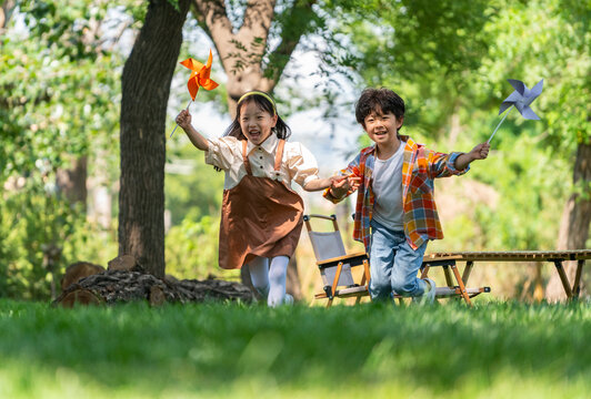 两个小孩子在草地上举着风车开心奔跑