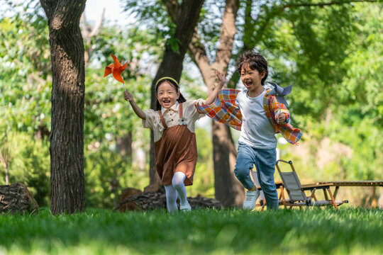 两个小孩子在草地上举着风车开心奔跑
