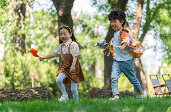 两个小孩子在草地上举着风车开心奔跑