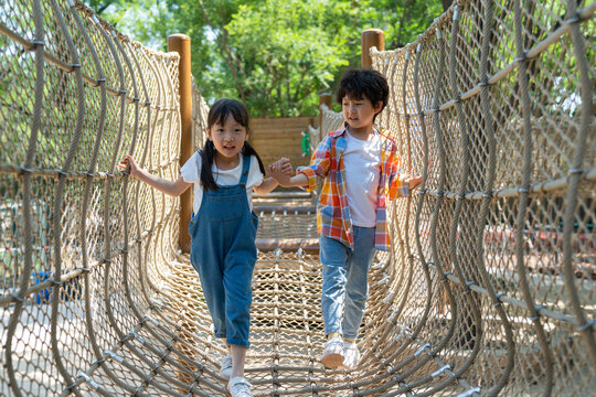 两个小孩子相互鼓励牵手走绳桥