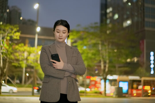 走在夜晚人行道上看手机的女性