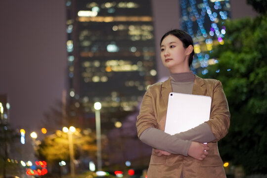 赋权女性手持电脑走在城市夜里