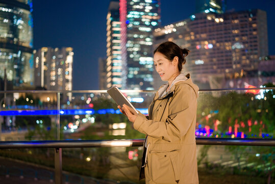 女性夜间与平板电脑对抗城市景观
