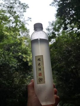 手捧糯米酒于绿意背景中