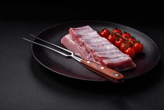 生猪肉肋排放在纹理混凝土背景上，撒有盐、香料和香草。生猪肉肋排上的肉撒有盐、香料和香草