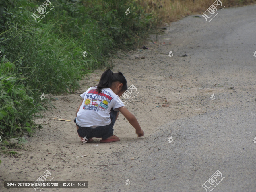 乡村道路边捡石子的女孩