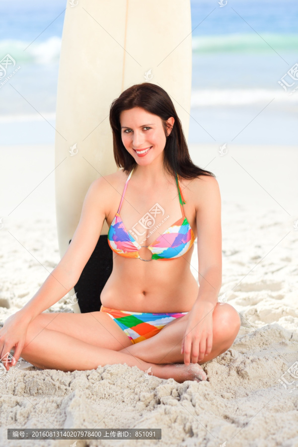 美女坐在沙滩上靠着冲浪板