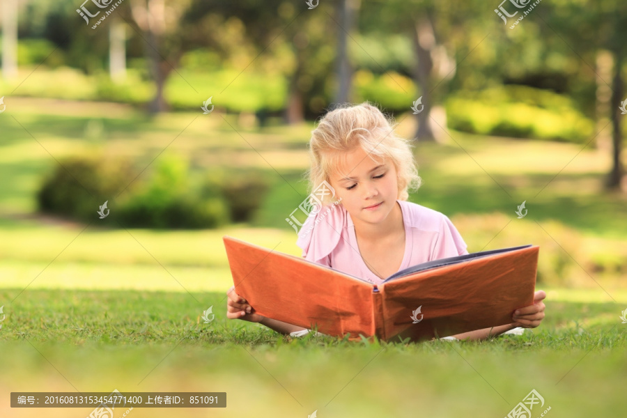 趴在草地上看相册的小女孩