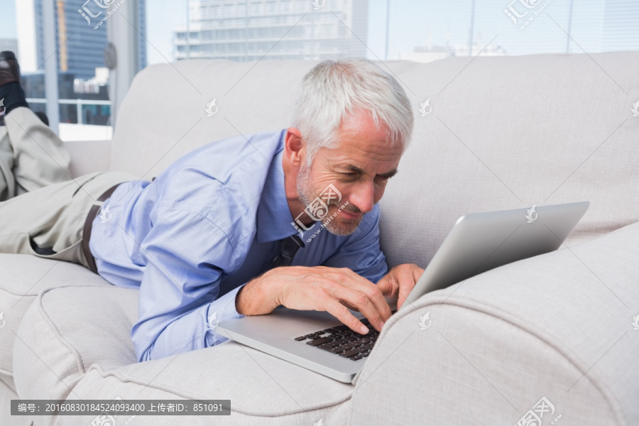 商人躺在沙发上使用笔记本电脑