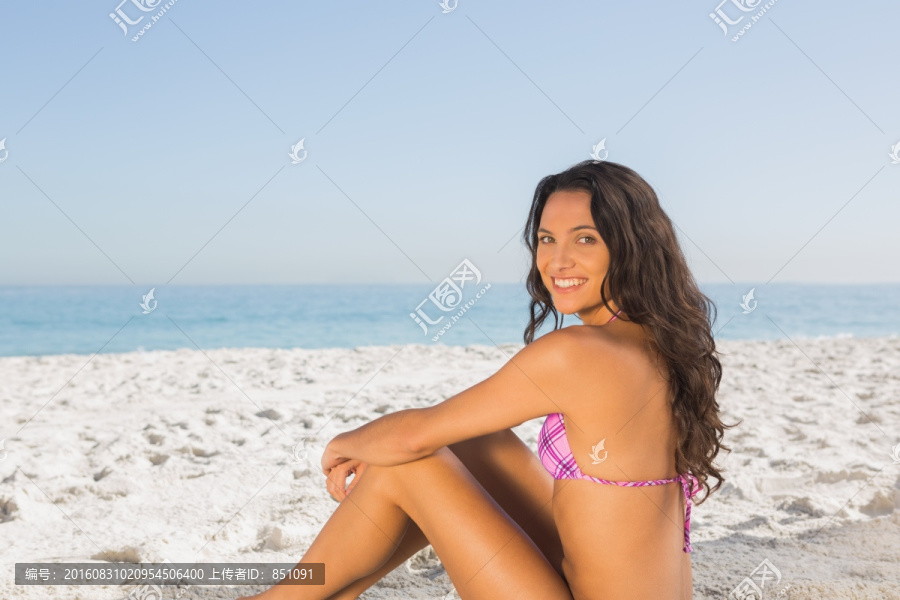 微笑的性感女人坐在沙滩上