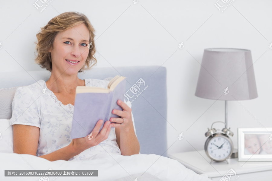 快乐的金发女子坐在床上看书书