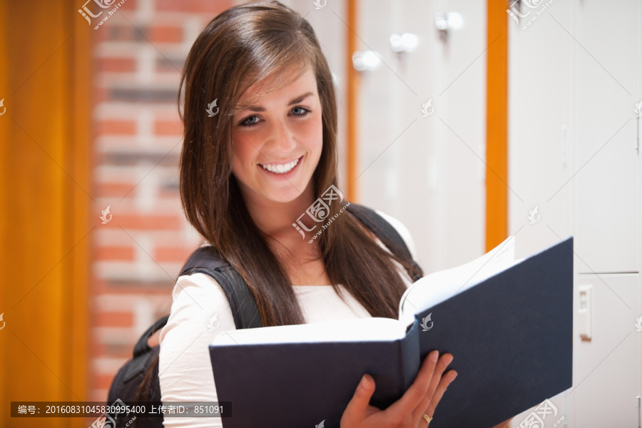 微笑的学生在走廊里拿着一本书