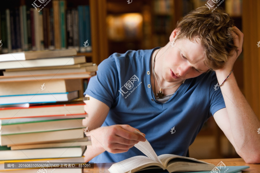 皱眉的男学生在图书馆里读一本书