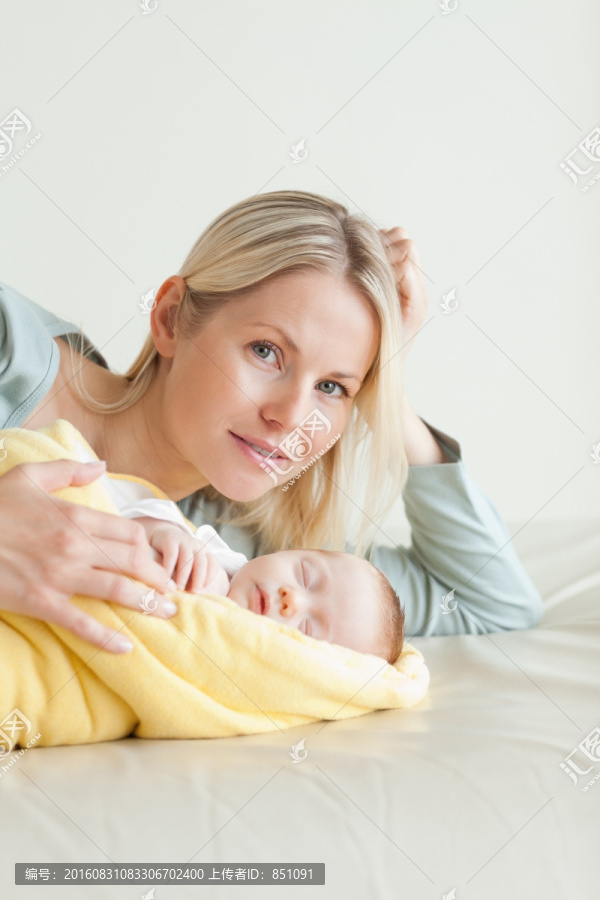 年轻的妈妈躺在她熟睡的婴儿旁边
