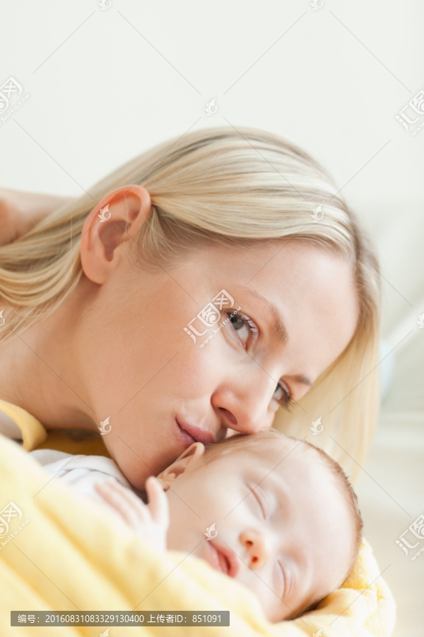 可爱的年轻母亲吻着她熟睡的婴儿