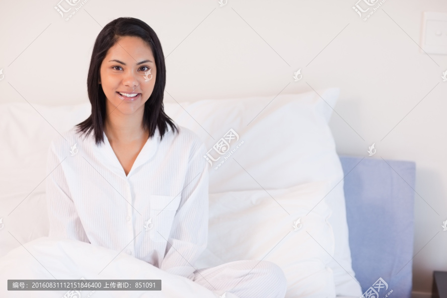 微笑的年轻女子穿着睡衣坐在床上