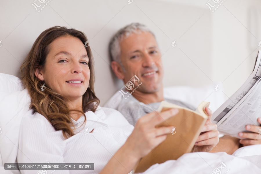 在床上看书和看报纸的夫妇