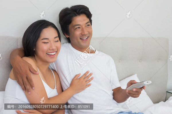 夫妇坐在床上微笑着看着电视