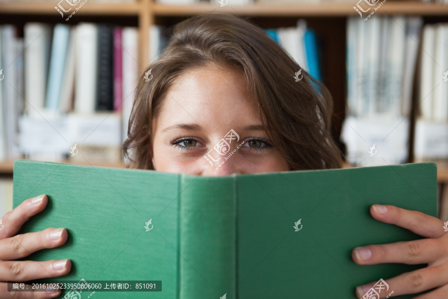 微笑女学生拿着书本在图书馆里