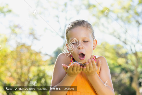 在公园里吹着手上的花瓣的女孩