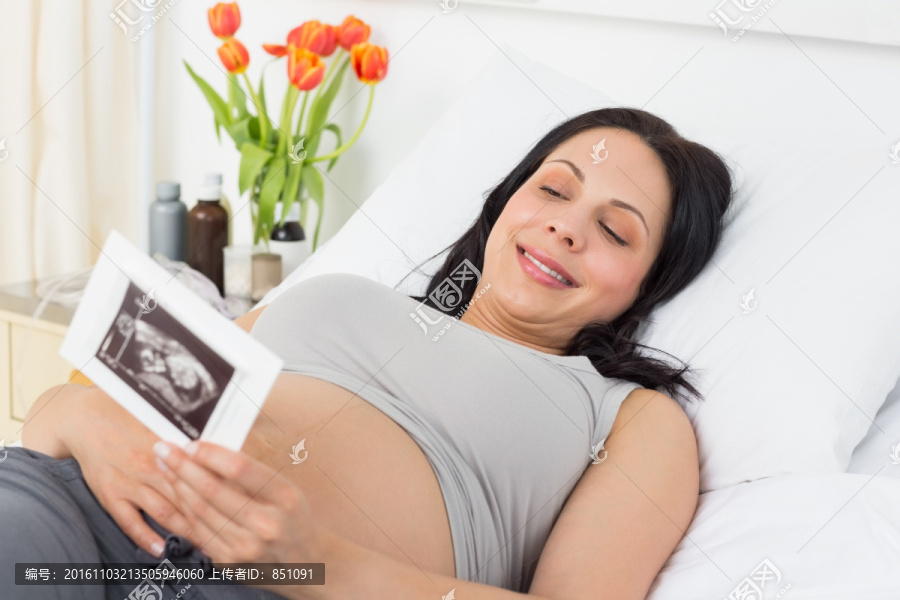 躺在病床上拿着超声照片的孕妇
