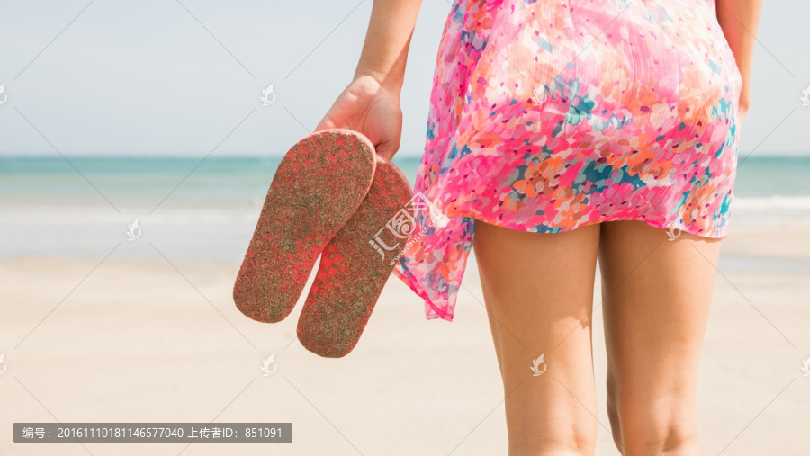 拿着拖鞋站在沙滩上的女人