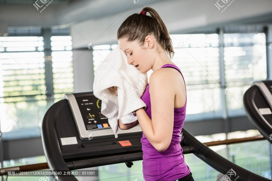 女人站在跑步机上用毛巾擦汗