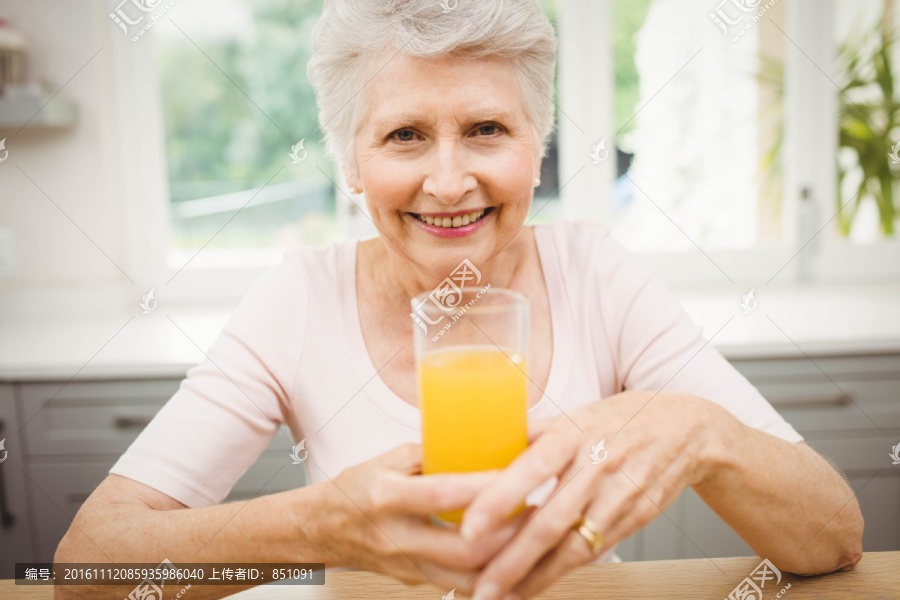 坐在餐桌前喝一杯橙汁的老太太