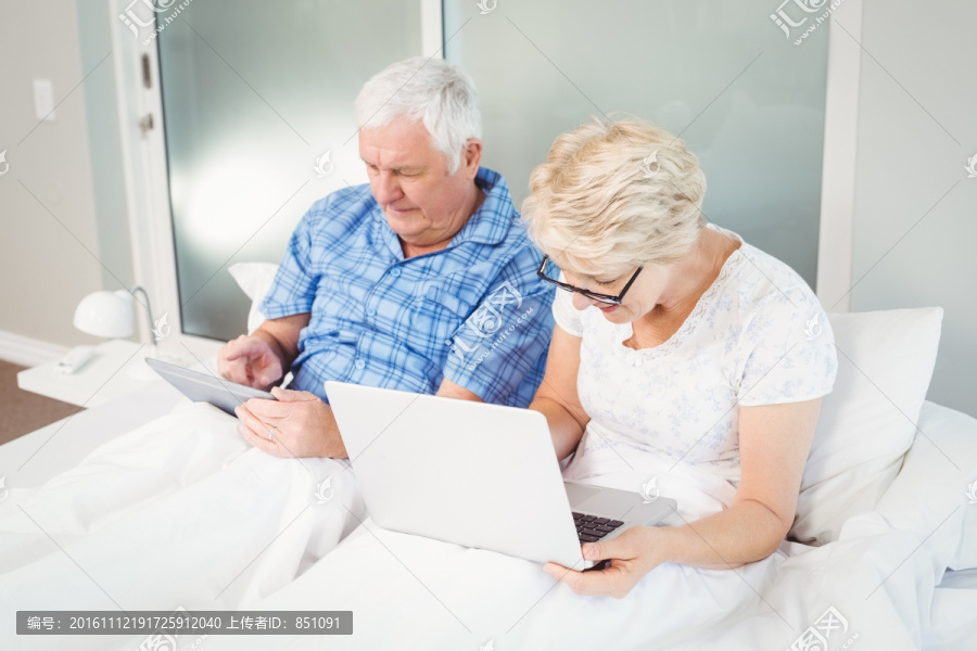 坐在床上使用电子设备的老夫妇