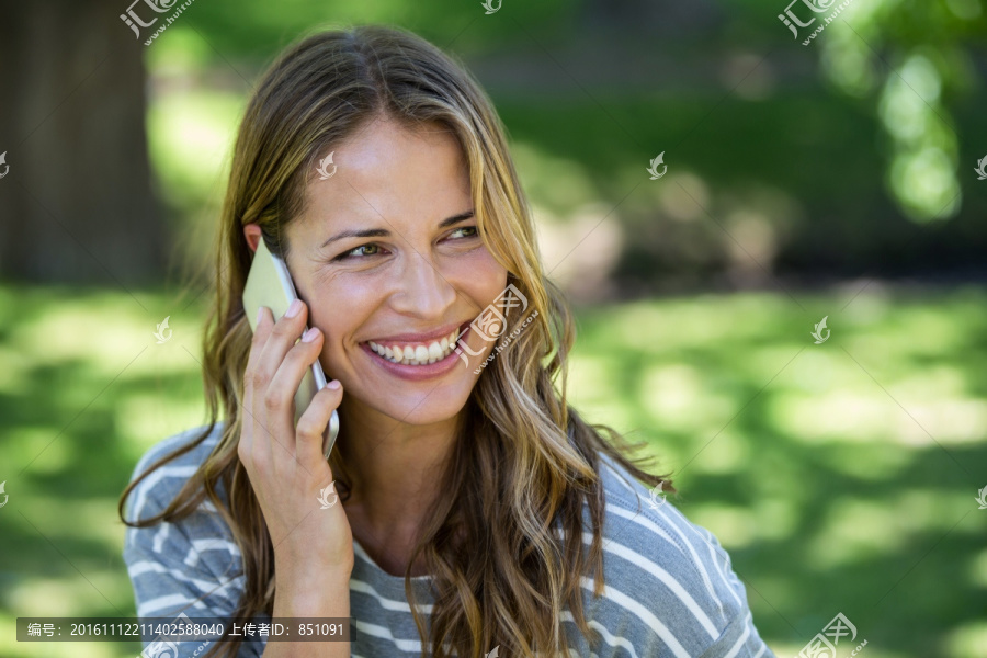 微笑的女人在公园里打电话