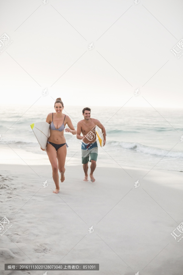拿着冲浪板在沙滩上奔跑的夫妇