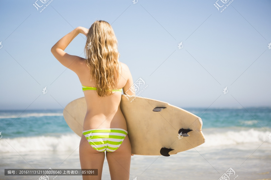 金发女子拿着冲浪板看着大海