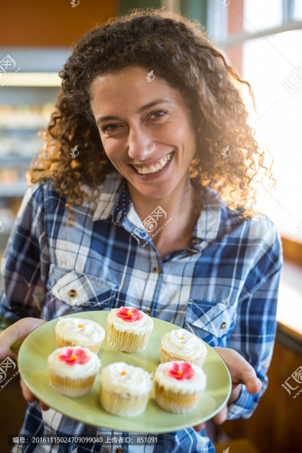 微笑的女人拿着一盘子纸杯蛋糕