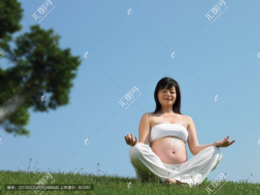 盘腿坐在草坪上练习瑜伽的孕妇